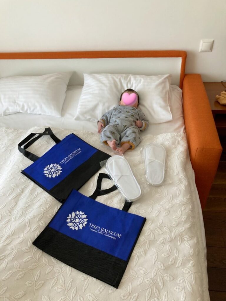 ハンガリー ティサ湖のTisza Balneum Hotelのソファーベッドに寝転ぶ娘　スリッパとホテルの手提げ袋