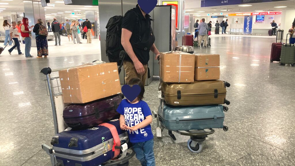 ブダペスト空港の到着ロビーで、スーツケースをカートに乗せて運ぶ夫と息子