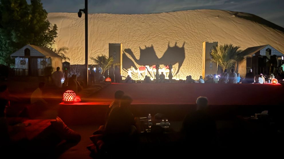 アブダビの砂漠ツアーのデザートキャンプで、ライトアップされた3頭のラクダの影と砂丘