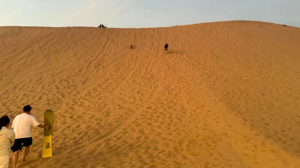 アブダビの砂漠ツアーのデザートキャンプで、サンドボードを持って砂丘をのぼる夫と息子