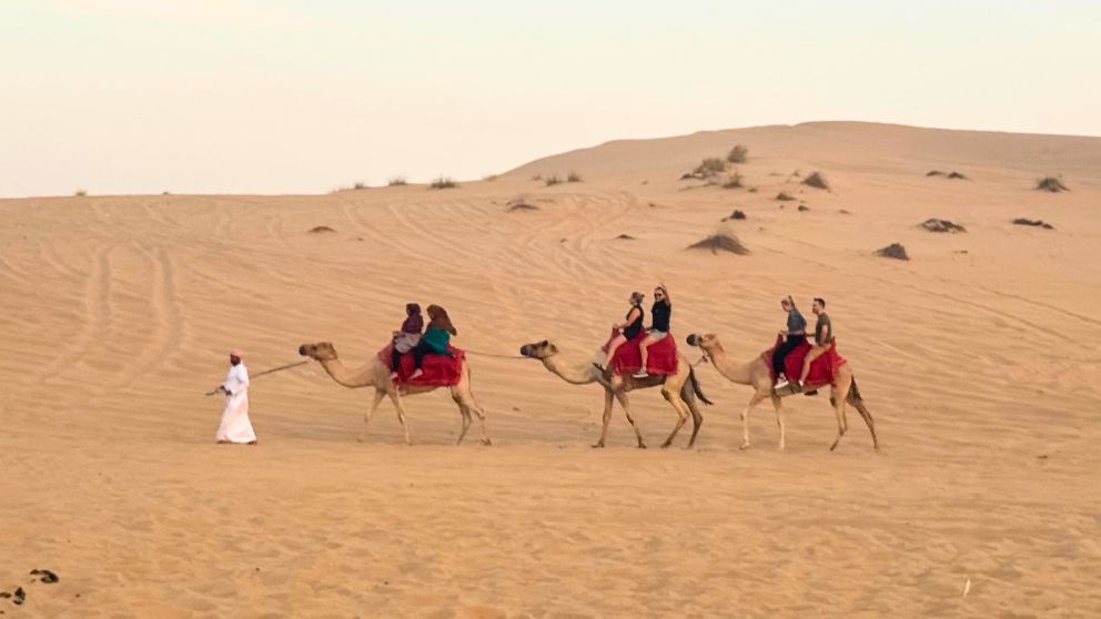 アブダビの砂漠ツアーのデザートキャンプでラクダに乗る人々と砂漠の風景