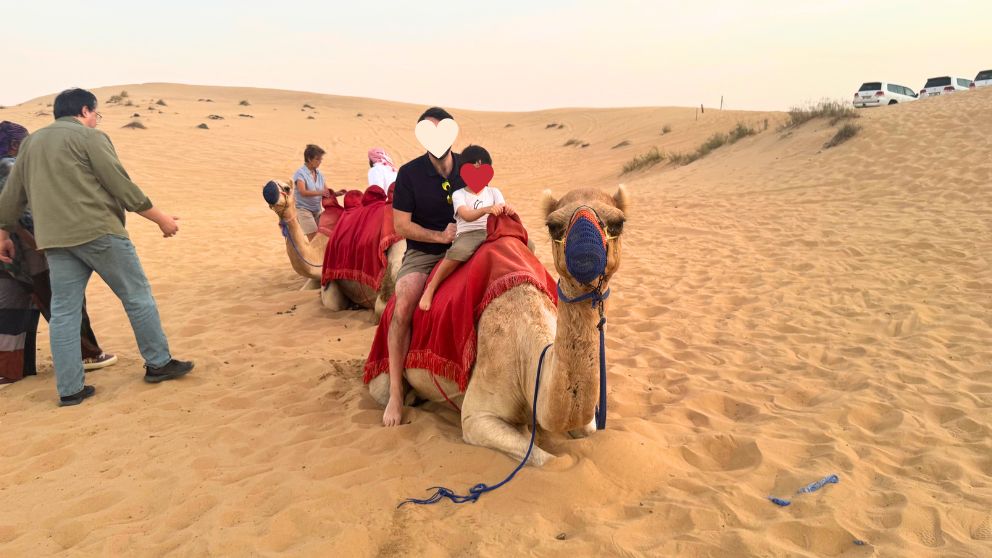 アブダビの砂漠ツアーのデザートキャンプでラクダに乗る夫と息子