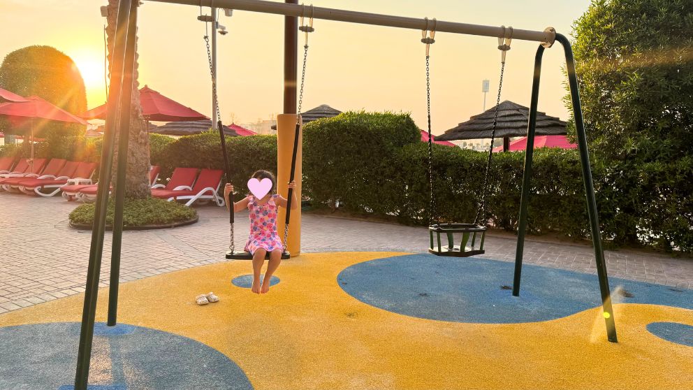 アブダビにあるホテルKhalidiya Palace Rayhaanのプールエリアにある子どもの遊び場でブランコに乗る娘