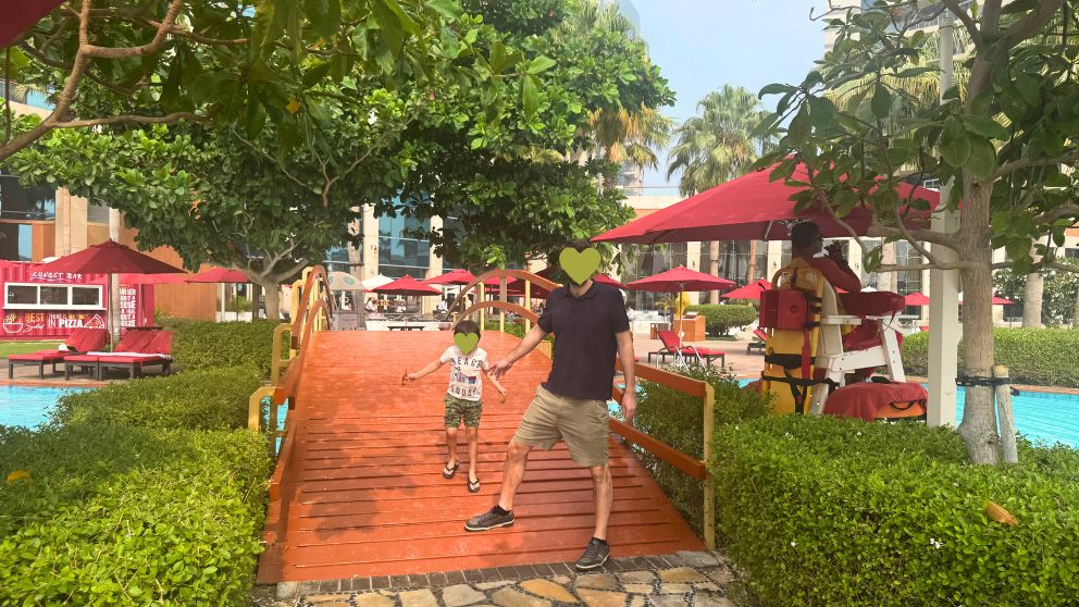 アブダビにあるホテルKhalidiya Palace Rayhaanのプールにかかる橋を渡る夫と息子