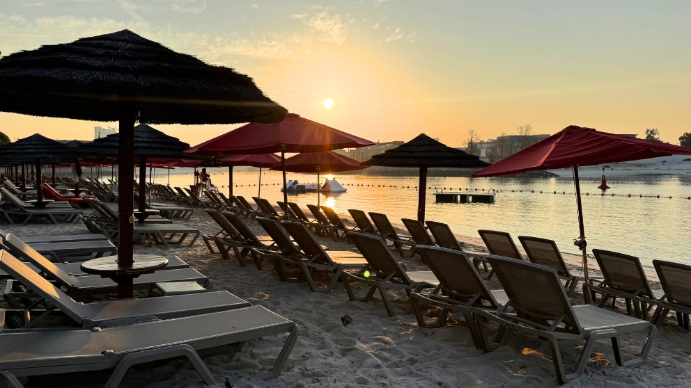 アブダビにあるホテルKhalidiya Palace Rayhaanのプライベートビーチに並ぶパラソルとビーチチェア。朝日がのぼっている