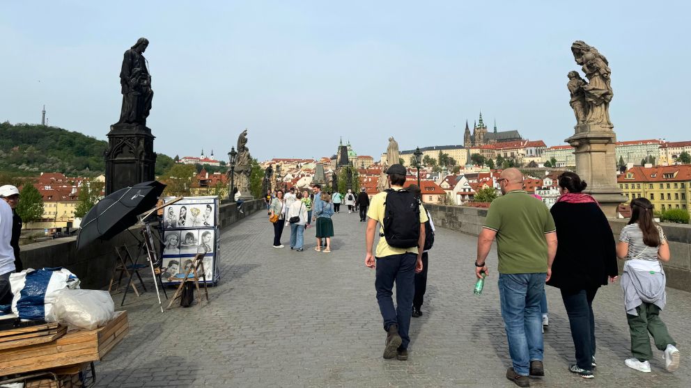 プラハのヴルタヴァ川(モルダウ川)にかかるカレル橋と、その上を歩く観光客の様子。背景にはオレンジ色の屋根瓦の建物が連なっている
