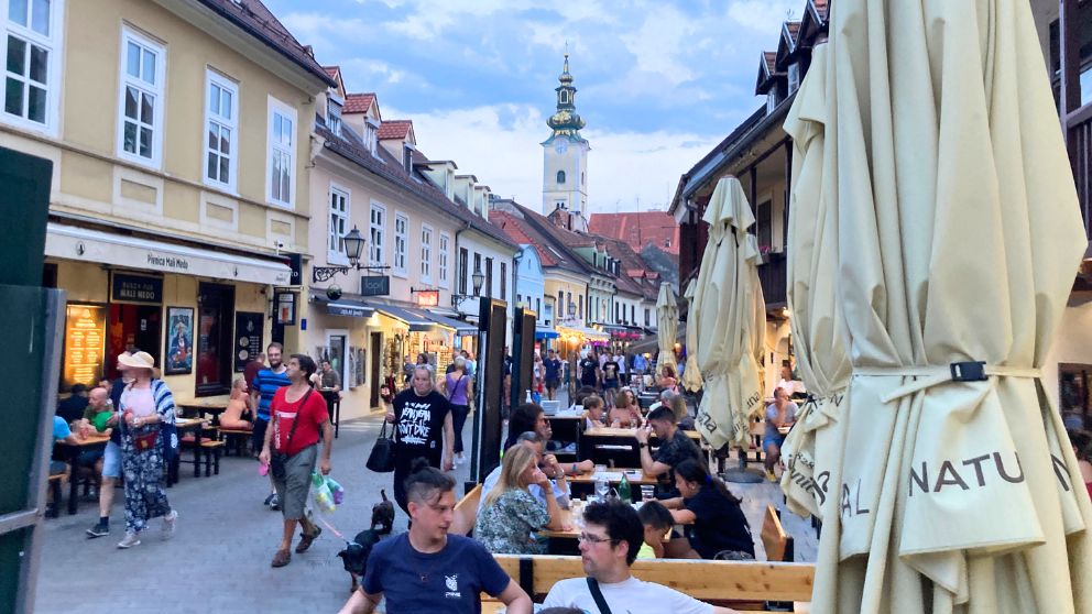 ザブレブのトカルチチェヴァ通りの夏の夕方の様子。カラフルな建物が並び、テラス席にお客さんがたくさん座っている