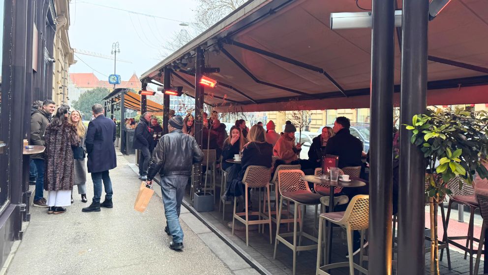 ザグレブの新市街のテラス席で、コートをきたままコーヒーや軽食をとる人々の様子