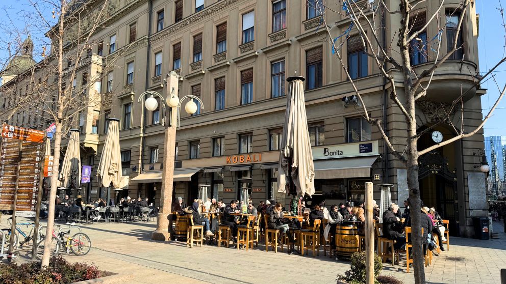 日の当たる新市街のテラス席で食事を楽しむ人々