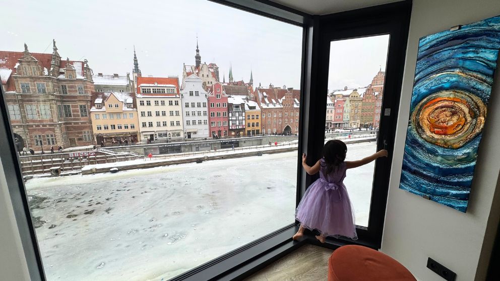 グダニスクのアパートの大きなガラス窓から見える、凍ったモトワヴァ川と細長い建物が並ぶ川沿いの風景