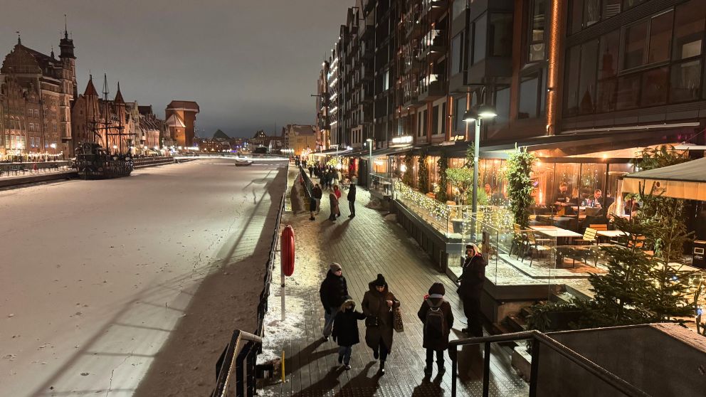 ポーランドのグダニスクのモトワヴァ川沿いの歩行者専用道路を歩く人々。レストランが並びテラス席が設けられている