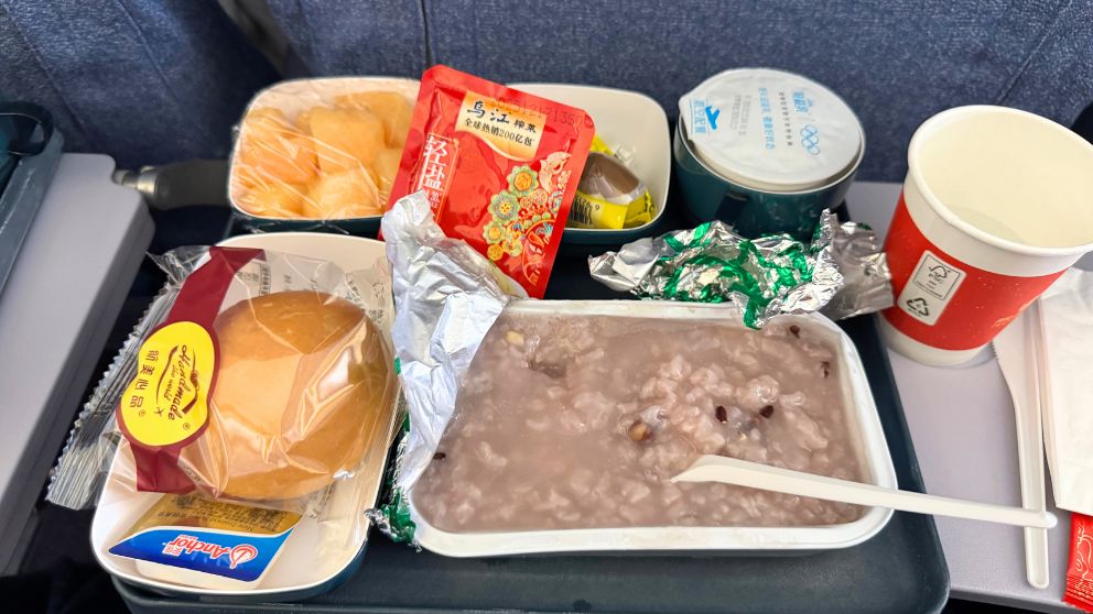 中国国際航空の機内食(北京→羽田のおかゆの朝食)。パン・フルーツ・ピータン・ザーサイもついている