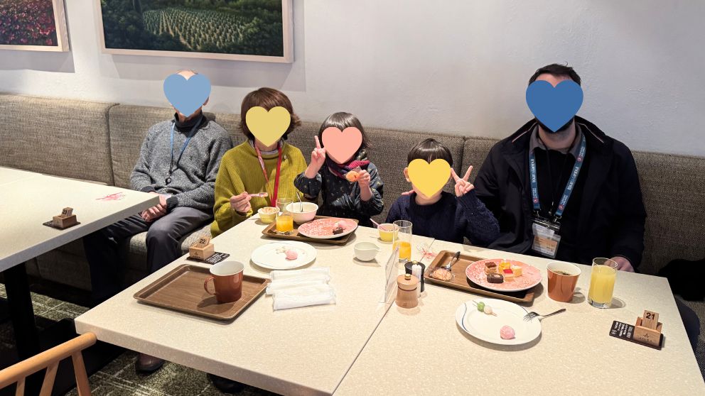 飛鳥Ⅱのレストラン(リドカフェ)で軽食をいただく、私の家族の集合写真。和モダンな内装の席で、それぞれがビュッフェで取ってきたジュースやデザートを楽しんでいる。子供たちがピースサインをしている
