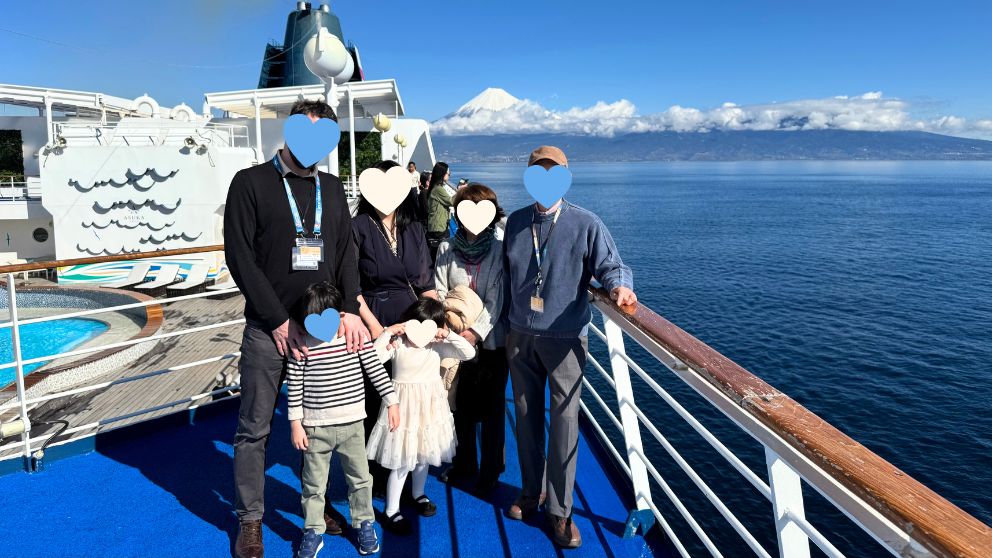 飛鳥Ⅱのオープンデッキにて、青空の下、3世代家族6人全員が揃った記念写真。窓の外の大海原には雄大な富士山がくっきりと見えている