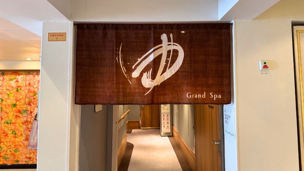 飛鳥Ⅱの展望大浴場「グランドスパ」の入り口付近。高級感のある和モダンな内装で、入り口には「Grand Spa」の文字と落ち着いた照明が配置されている