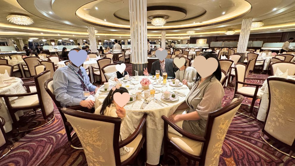 華やかな照明のメインダイニング「フォーシーズン」で、夕食のフルコースを楽しむ家族の様子。テーブルにはパンやビール、美しい花が飾られている