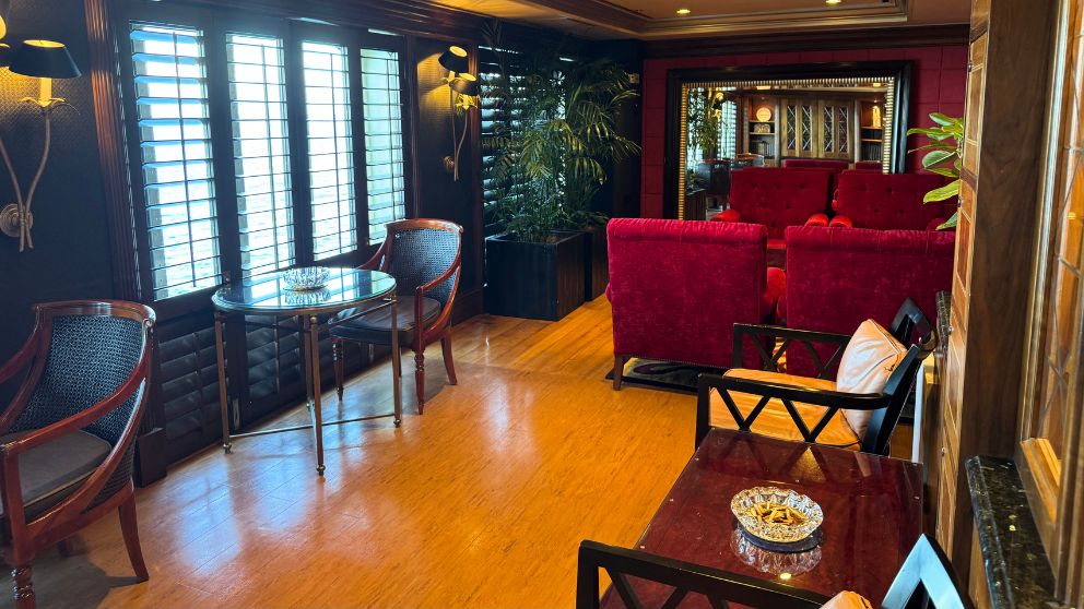 飛鳥Ⅱのスモーキングラウンジ。木目調の床と暗めの壁、赤いアンティーク風の椅子が並ぶ、落ち着いた大人の空間