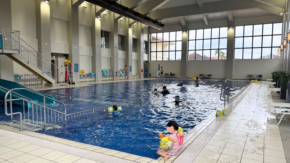フサキビーチリゾートの広々とインドアプール、娘がアームリングをつけてプールサイドに座っている