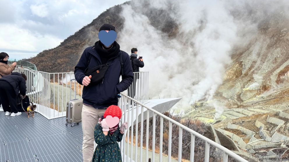大涌谷の噴煙が上がる火山地帯を背景に記念撮影する夫と娘