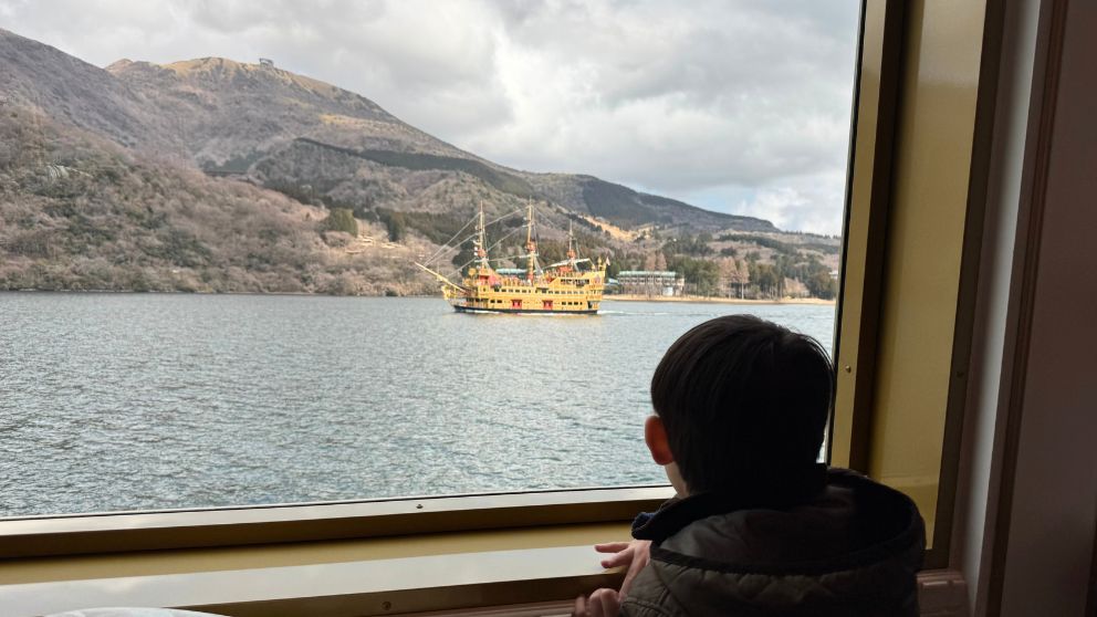 海賊船の窓から見下ろす、芦ノ湖の青い水面とすれ違う別の黄色の海賊船