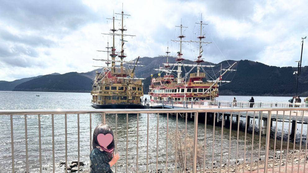 芦ノ湖の桟橋に停泊する、豪華な装飾が施された箱根海賊船と湖畔に立つ子供。