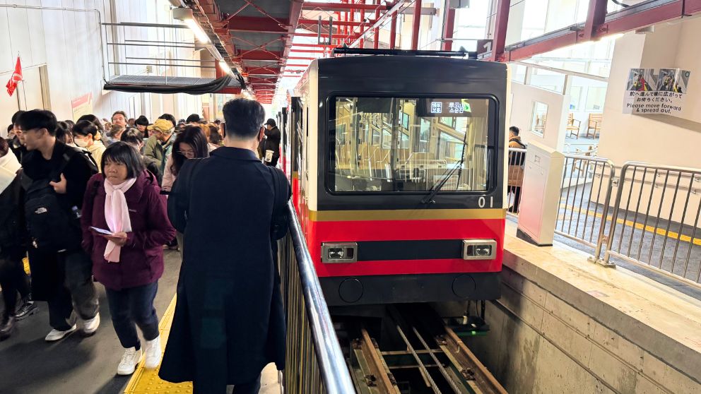 箱根登山ケーブルカーの強羅駅ホームに停車する、赤と黒のツートンカラーの新型車両(ケ100・200形)。乗車を待つ多くの観光客の様子