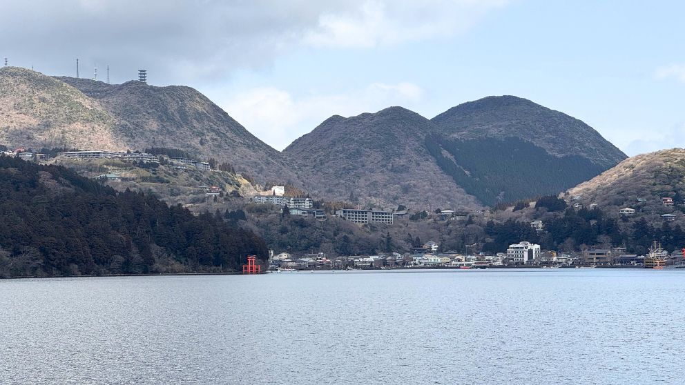 海賊船から眺める、芦ノ湖の対岸に立つ箱根神社の平和の鳥居と湖畔の街並み