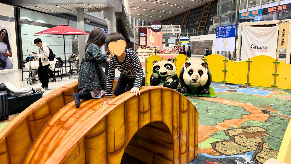 北京首都国際空港の遊び場で橋の上に乗って遊ぶ子どもたち。奥にパンダの置物が見える