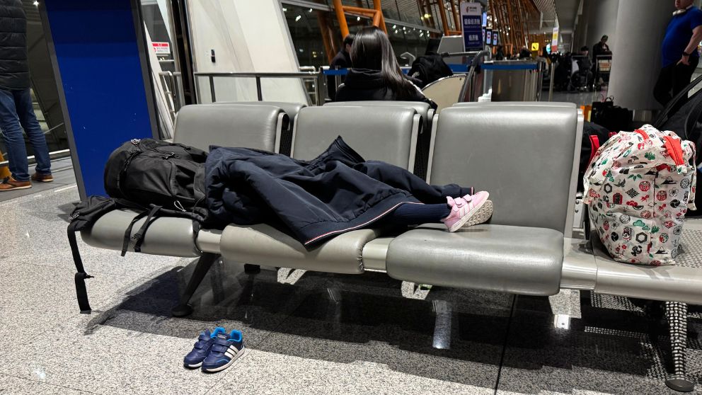 北京首都国際空港のトランジットエリアで椅子に横になって休む娘