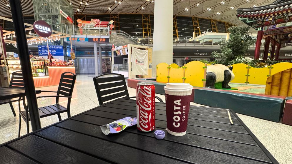 北京首都国際空港のCosta Coffeeのテーブルにコーヒーとコーラ。奥に子ども向け遊び場が見える
