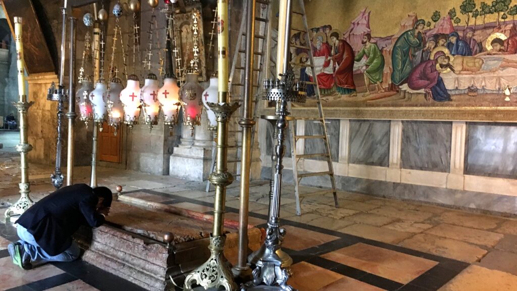 聖墳墓教会の内部。キャンドルや装飾品が並ぶ荘厳な空間で信者が祈りを捧げている