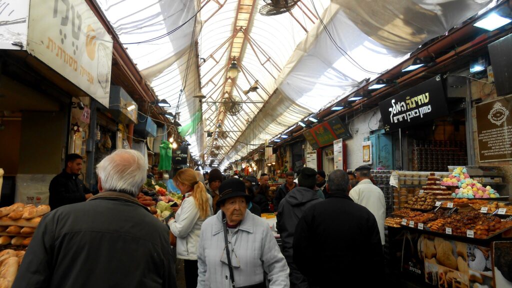 エルサレムのマハネ・イェフダ市場のアーケード。白い天幕の下を買い物客が行き交う活気ある様子