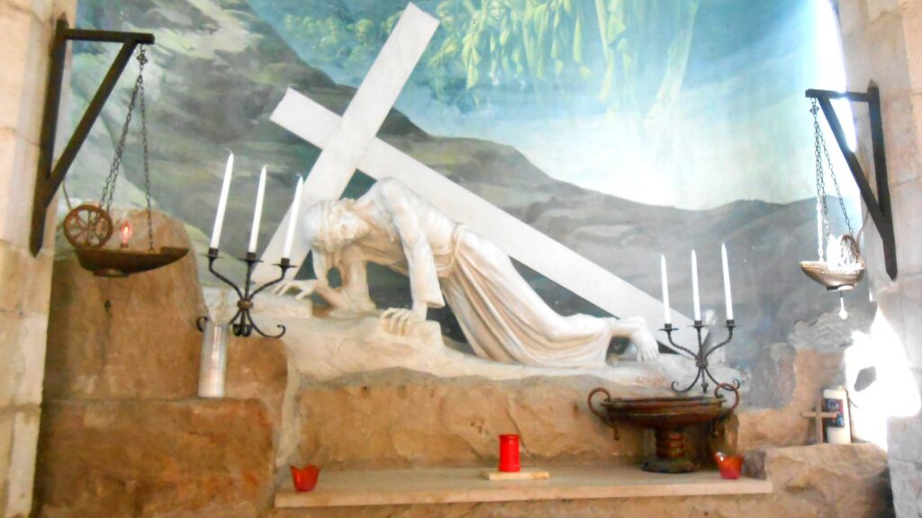 悲しみの道のステーション。十字架の重さで倒れ込むイエスの白い彫刻と、背後に描かれた天使たちの壁画