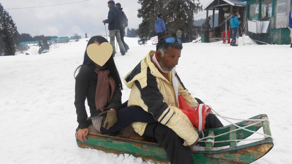 インド屈指のスキーリゾート、グルマルグの雪原で地元の案内人と木製のそりに乗る体験