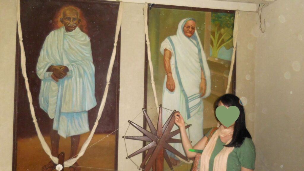 ラージコットのカバ・ガンジー・ノ・デロでチャルカを回す。ガンジーと母プトリバイの肖像画の前で