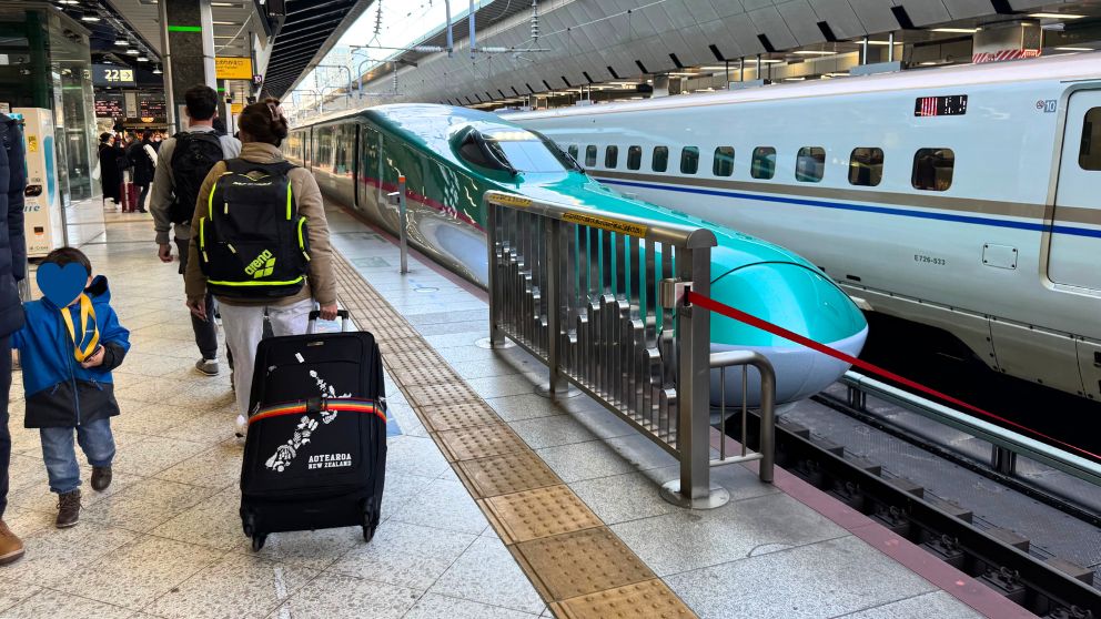 東京駅のホームを歩く息子。エメラルドグリーンの東北新幹線がホームに入ってきたところ