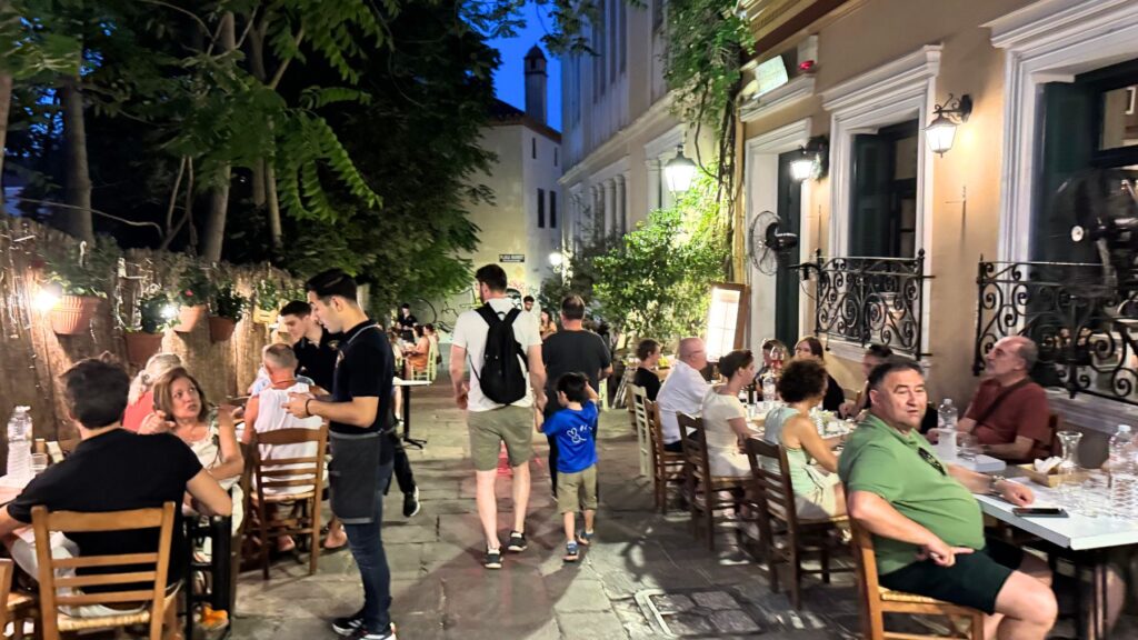 夜のプラカ地区でにぎわうレストランの屋外席と石畳の路地