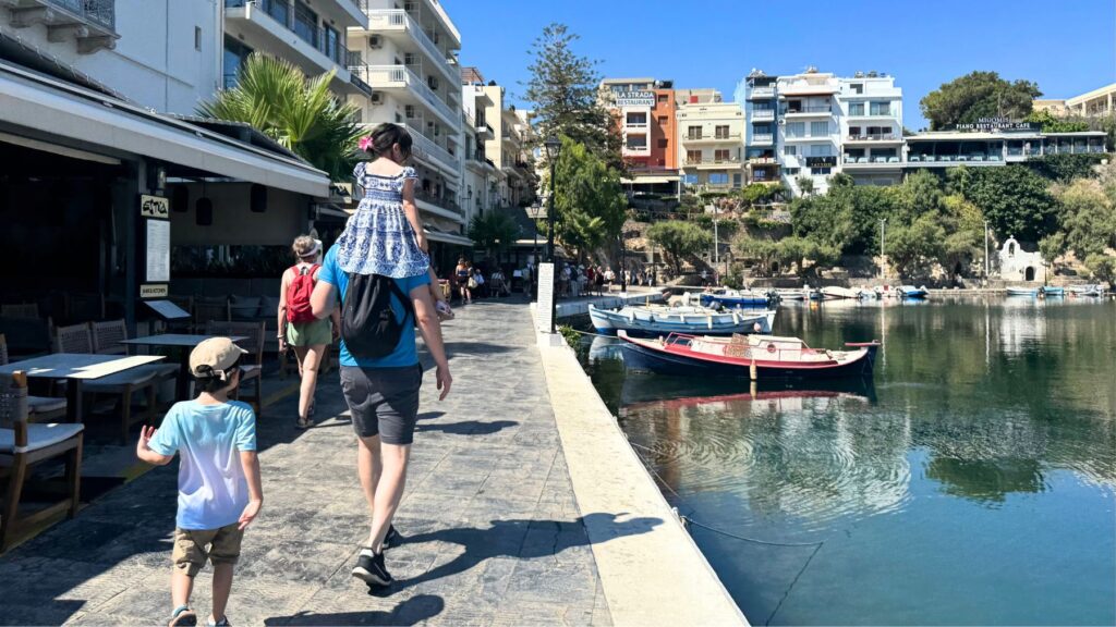 アギオス・ニコラオスのヴルリスメニ湖畔を歩く家族。湖を囲むカラフルな街並みとボート