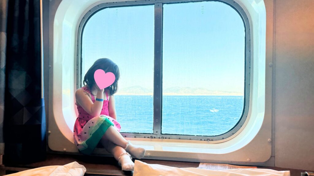 窓辺に腰掛けてエーゲ海の景色を眺める子ども