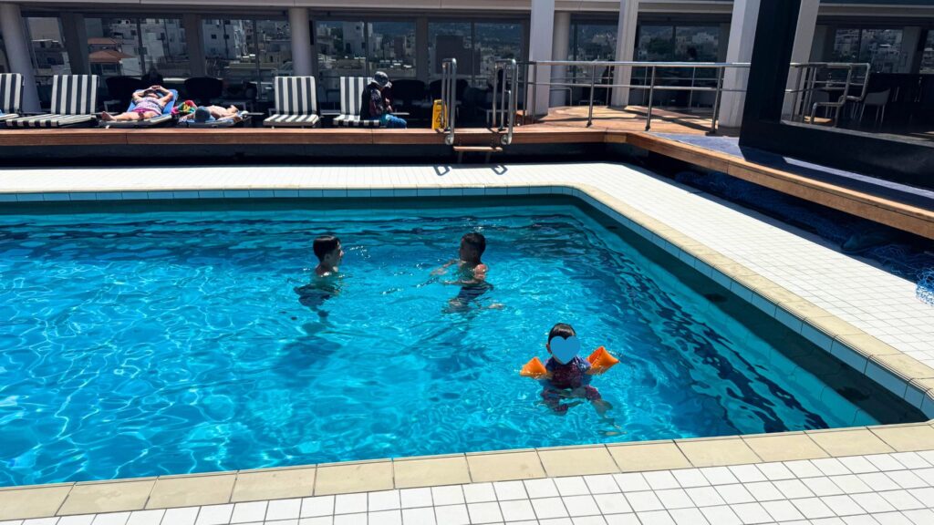 11デッキHalara Coveの海水プールで泳ぐ子どもと大人。奥にサンチェアと港の街並み