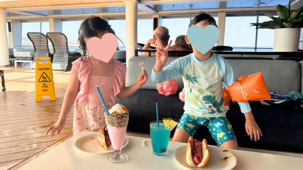 デッキのラウンジでホットドッグとカラフルなドリンクを楽しむ子どもたち