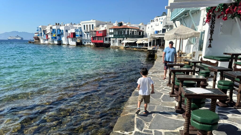海沿いの遊歩道を歩く息子とカラフルな家々が並ぶミコノスのリトル・ベニス