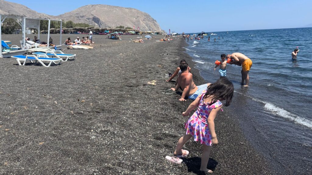 ペリッサの黒い砂浜で波打ち際を歩く娘
