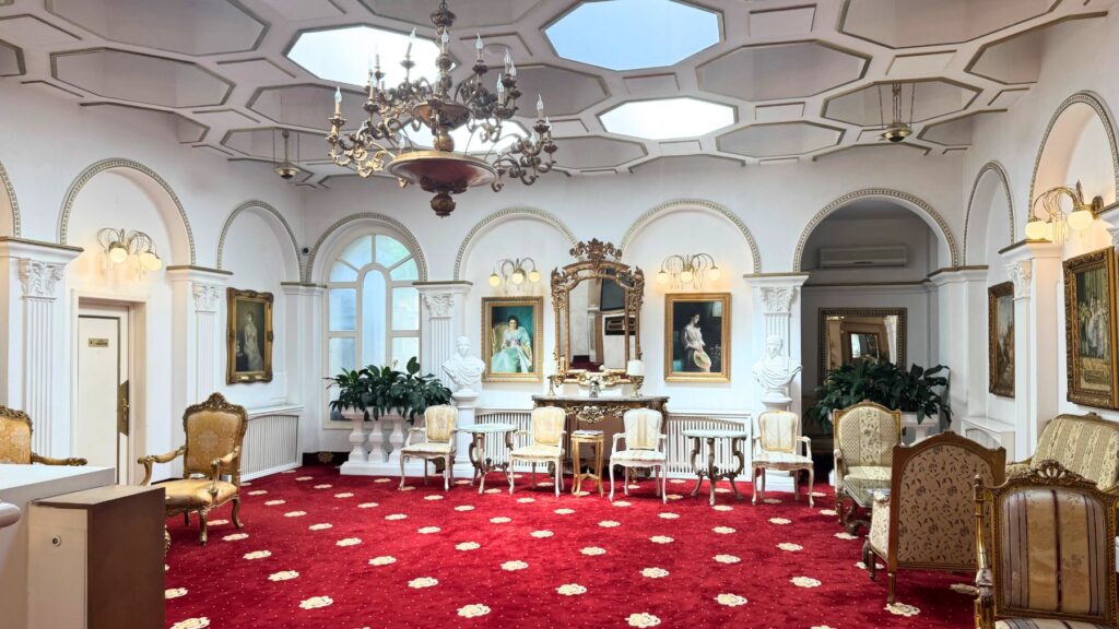 Hotel Împăratul Romanilor のサロン。赤い絨毯に金の椅子、肖像画と大きな鏡、天井のガラス天窓