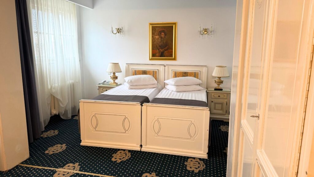 Hotel Împăratul Romanilor の客室。白い家具のツインベッドと紺色の絨毯、肖像画とシャンデリア
