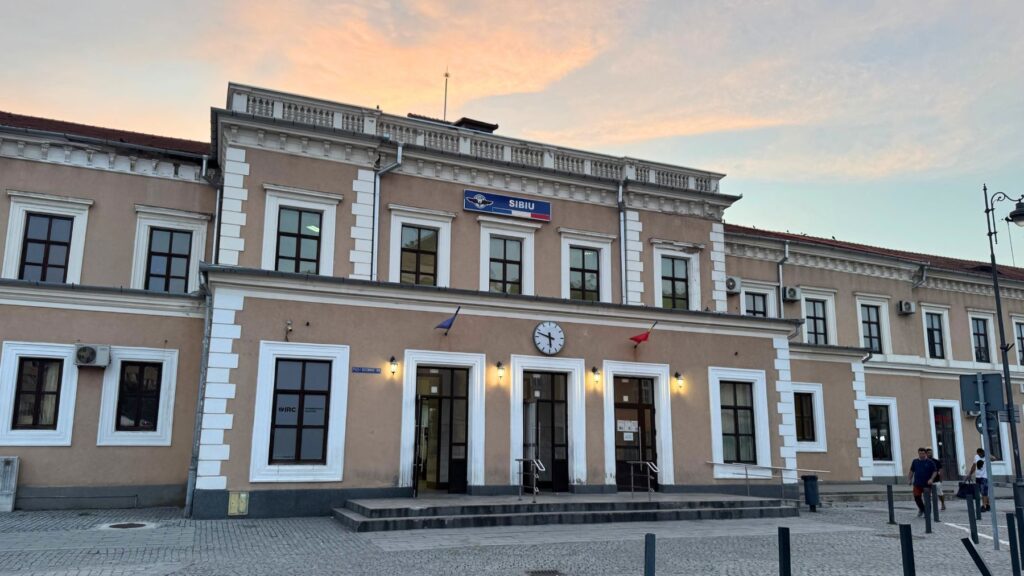 夕暮れのシビウ駅の駅舎。「SIBIU」の看板と時計のある、クリーム色のクラシックな建物