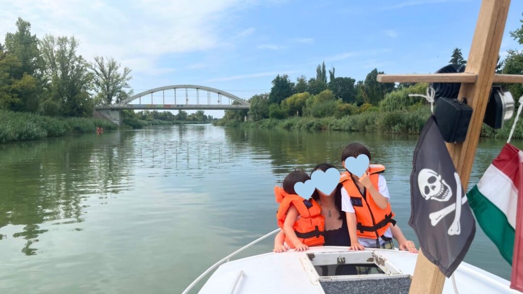 ライフジャケット姿の母と3人の子ども、奥に白いアーチ橋