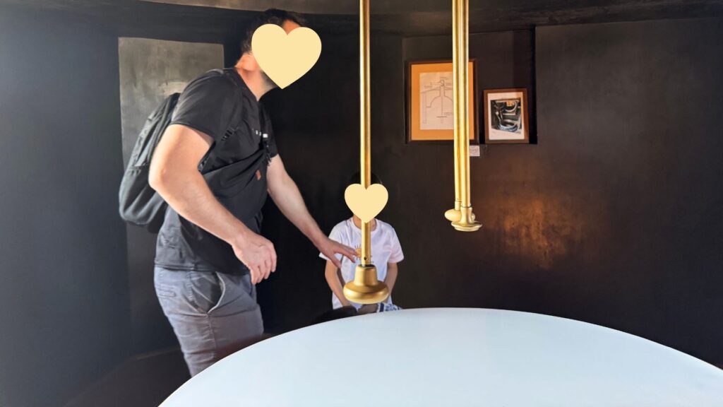 リツェウム最上階のカメラ・オブスクラ(暗箱)の部屋。暗い室内の中央に白い円卓があり、天井の反射鏡で町の様子が映し出される
