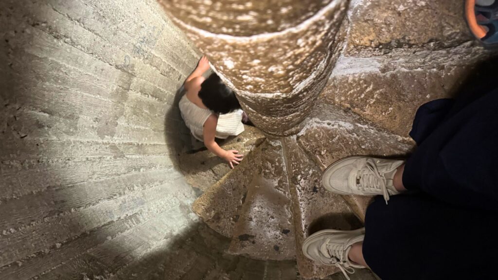 ミナレット内部の薄暗く狭いらせん階段。子どもが手すりの中心をつかみながらのぼる