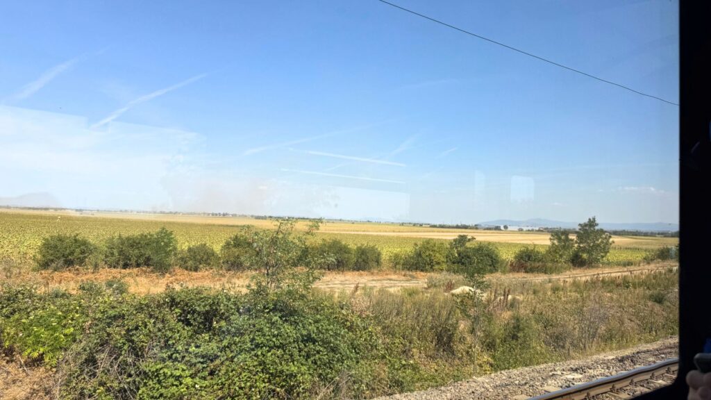 列車の車窓から見えるハンガリーの田園風景。畑が広がる平原と、遠くにかすむ山並み